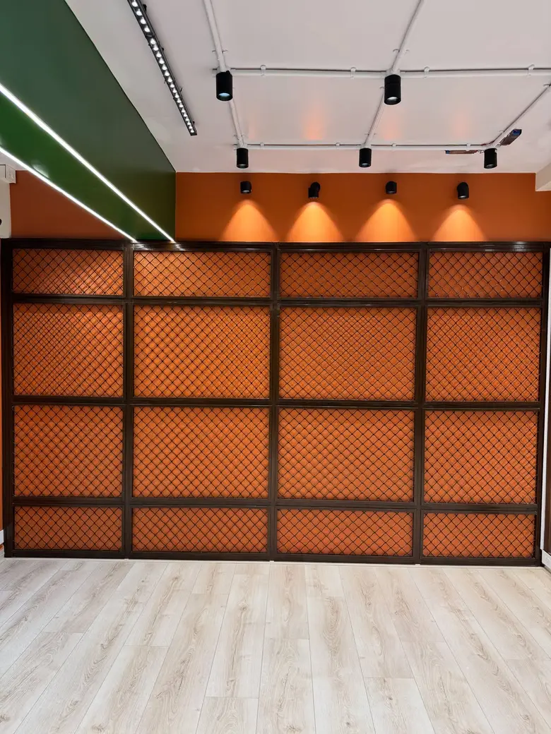 Orange wall with dark grill mesh panels lit by warm spotlights at P Square Studio